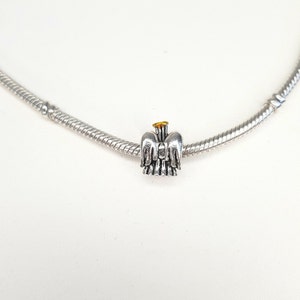 May include: A silver charm bracelet with a silver angel charm with gold accents.