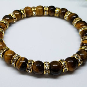 May include: A brown tiger's eye gemstone bracelet with gold accents and clear crystal beads.