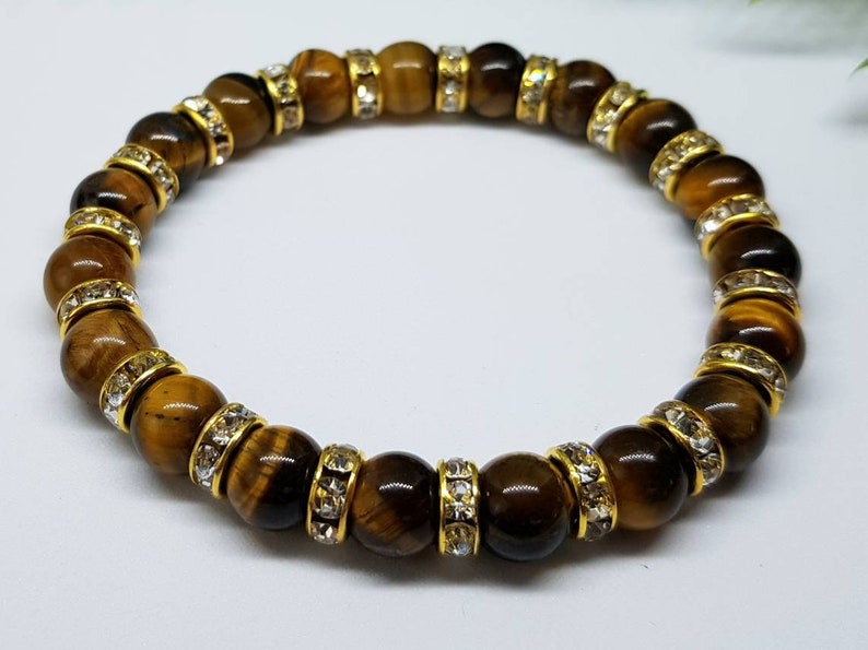 May include: A brown tiger's eye gemstone bracelet with gold accents and clear crystal beads.
