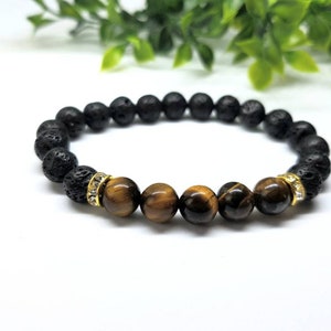 Puede incluir: Un brazalete de cuentas de lava negra y ojo de tigre con detalles dorados.