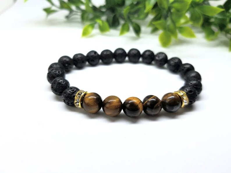 Puede incluir: Un brazalete de cuentas de lava negra y ojo de tigre con detalles dorados.