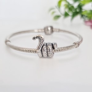 Puede incluir: Un brazalete de plata con un dije de serpiente de plata. La serpiente está enroscada y tiene una superficie texturizada detallada.