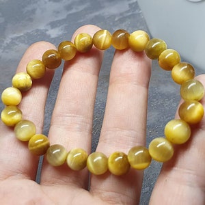 Peut inclure: Un bracelet compos&eacute; de perles de &oelig;il de tigre dor&eacute;es. Les perles sont rondes et ont une finition lisse et polie.