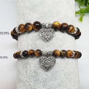 May include: Two tiger's eye stone bracelets with silver heart charms. The top bracelet has 8mm beads and the bottom bracelet has 6mm beads.