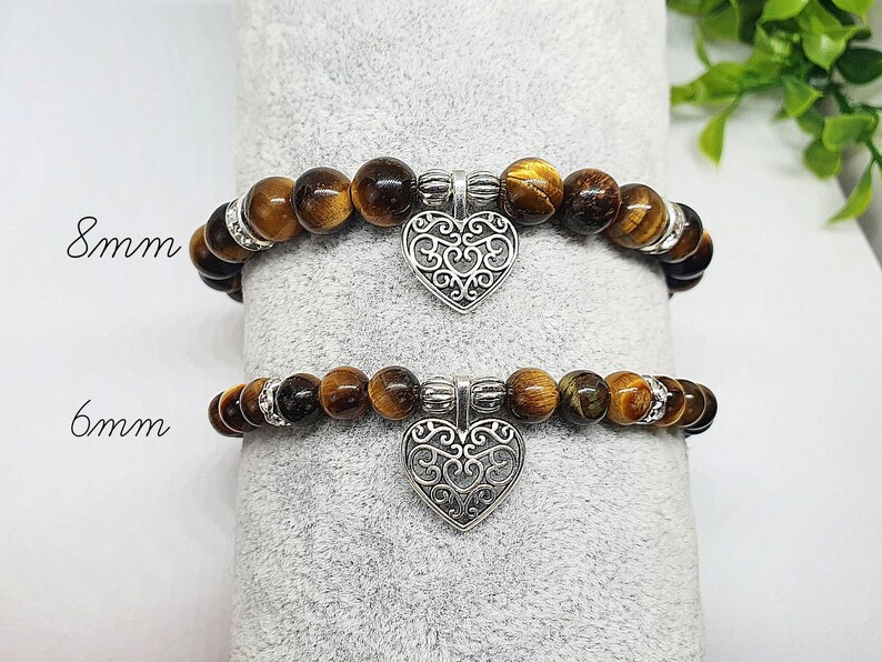 May include: Two tiger's eye stone bracelets with silver heart charms. The top bracelet has 8mm beads and the bottom bracelet has 6mm beads.