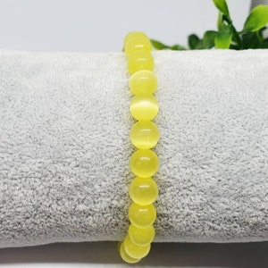 May include: A yellow gemstone bracelet with round beads. The bracelet is on a gray, fuzzy surface.