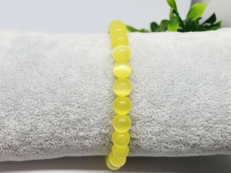 May include: A yellow gemstone bracelet with round beads. The bracelet is on a gray, fuzzy surface.