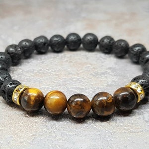 Puede incluir: Un brazalete de cuentas de lava negra y ojo de tigre con detalles dorados. El brazalete tiene una banda el&aacute;stica y est&aacute; hecho con piedras naturales.