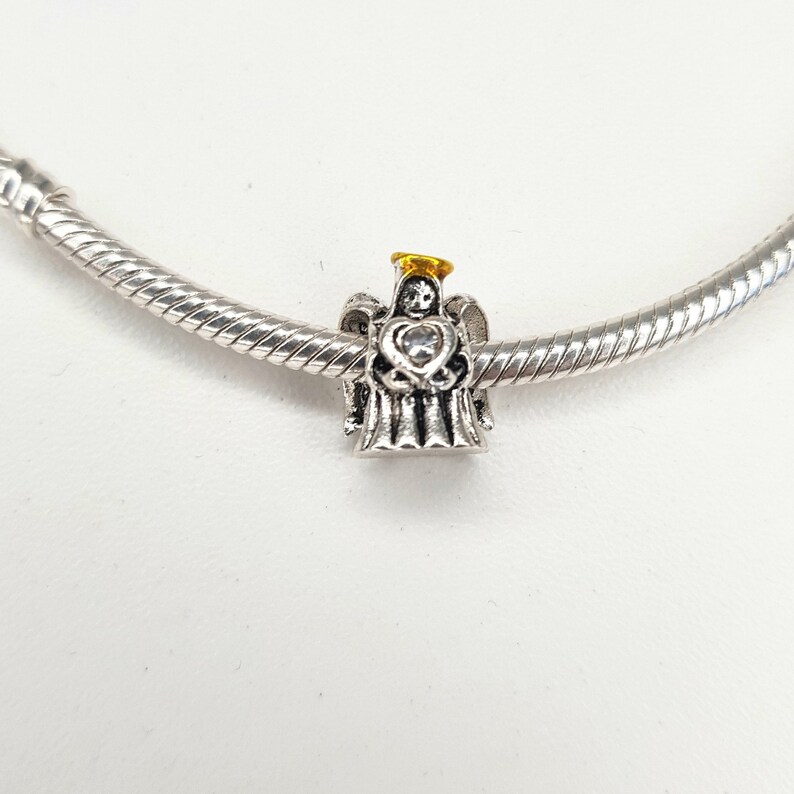May include: Silver charm bracelet with a silver angel charm holding a heart with a clear rhinestone. The angel has a gold halo.