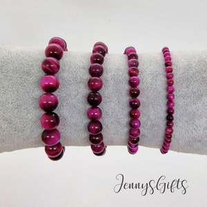 May include: Four pink tiger's eye gemstone bracelets of varying sizes. The bracelets are made with round beads and are displayed on a gray surface.