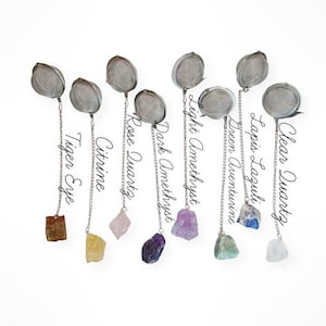 May include: Eight crystal tea infusers with different coloured crystals hanging from silver chains. The crystals are: clear quartz, lapis lazuli, green aventurine, light amethyst, dark amethyst, rose quartz, citrine, and tiger eye.