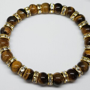 May include: A brown tiger's eye beaded bracelet with gold accents and clear crystal accents.