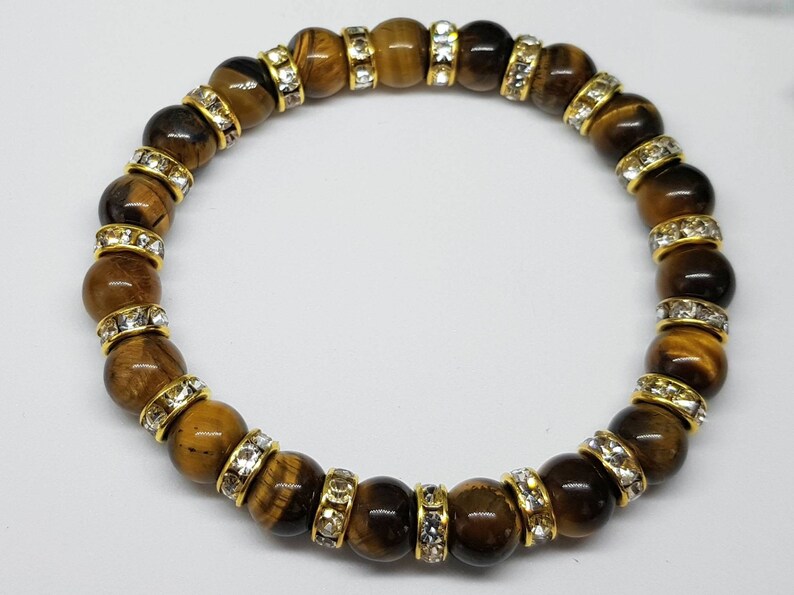 May include: A brown tiger's eye beaded bracelet with gold accents and clear crystal accents.