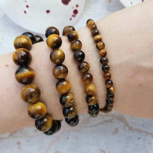 Puede incluir: Cuatro pulseras elásticas hechas de cuentas de piedra preciosa ojo de tigre pulidas. Las pulseras presentan tamaños de cuentas variables, desde esferas grandes y prominentes hasta cuentas más pequeñas, todas con el característico brillo dorado.