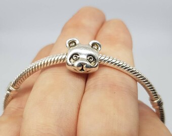 May include: A silver-colored charm featuring a panda bear head with black eye details. The charm is attached to a silver bracelet with a coiled design. The panda has a smiling expression.