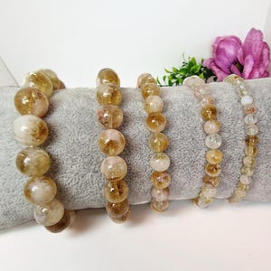 Könnte beinhalten: Vier Armbänder aus goldenen Citrinperlen. Die Perlen sind rund und durchscheinend. Die Armbänder sind in einer Reihe auf einer grauen Oberfläche angeordnet.