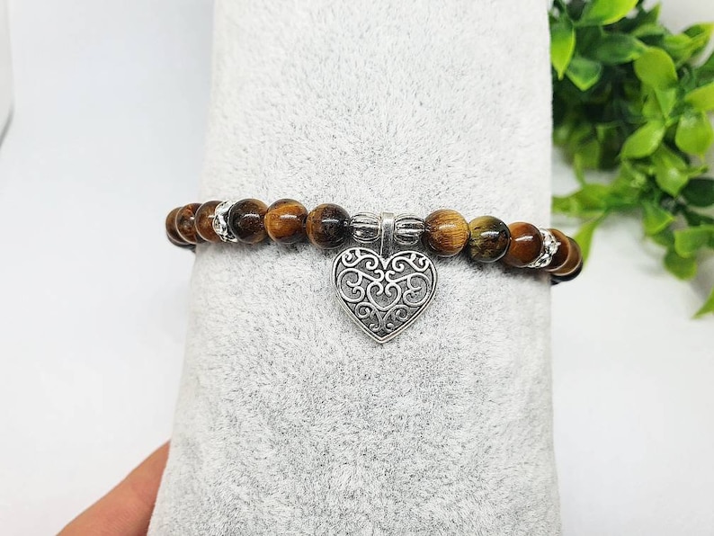 May include: A brown and gold tiger's eye beaded bracelet with a silver filigree heart charm.