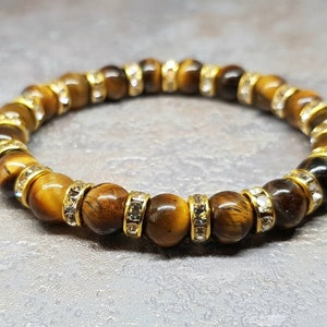 May include: A brown tiger's eye gemstone bracelet with gold accents and clear crystal beads.