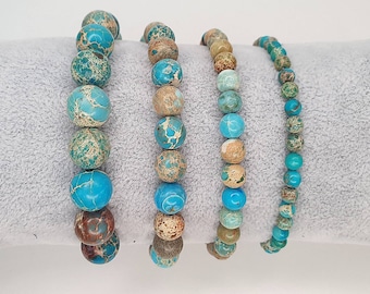 May include: Four turquoise and brown jasper beaded bracelets stacked on a gray fabric surface. The bracelets are made of round beads with a mottled pattern.
