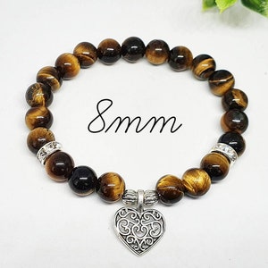 May include: A brown and gold tiger's eye beaded bracelet with a silver heart charm. The beads are 8mm in size.