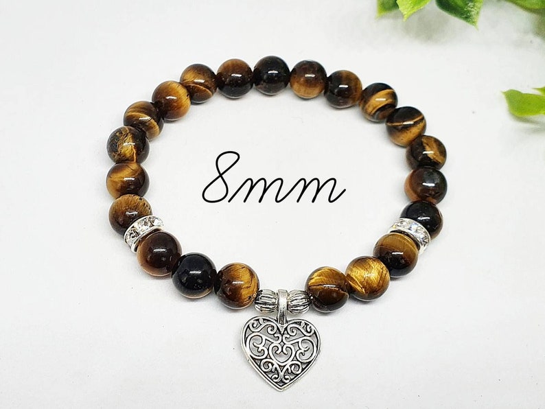 May include: A brown and gold tiger's eye beaded bracelet with a silver heart charm. The beads are 8mm in size.