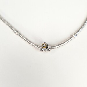 May include: A silver charm bracelet with a silver charm featuring a small, clear crystal surrounded by a gold ring.