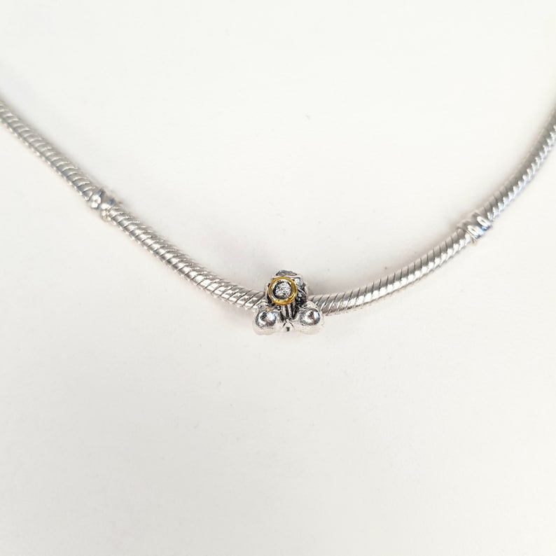 May include: A silver charm bracelet with a silver charm featuring a small, clear crystal surrounded by a gold ring.