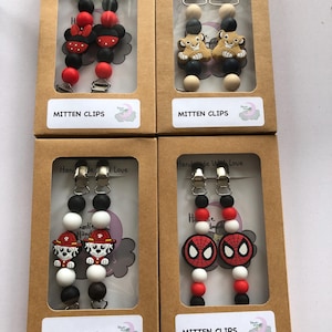 May include: Four sets of colorful silicone baby mitten clips with different character designs. Each set includes two clips with black and white beads, and a character charm. The characters are Mickey Mouse, Simba from The Lion King, a Paw Patrol character, and Spiderman.