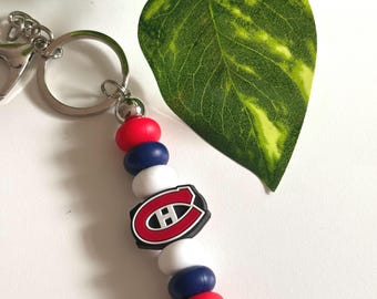 May include: A keychain featuring a series of red, white, and blue silicone beads arranged vertically. A central black, red, and white emblem displays the letter H inside a stylized C shape. The beads are attached to a silver metal ring and clasp.