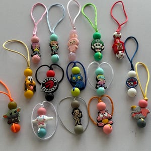 May include: A selection of beaded lanyards with cartoon character charms. Each lanyard has a loop for attaching to keys or other items. The beads are in various colours, including pink, green, blue, and yellow.
