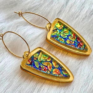 Puede incluir: Un par de pendientes dorados con un diseño único. Cada pendiente presenta una forma triangular con un patrón colorido tipo mosaico en tonos azules, verdes, amarillos y rojos. Los pendientes tienen un cierre de aro.