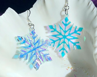 May include: A pair of iridescent snowflake earrings with silver hooks. The snowflakes are a light blue color with a holographic finish.