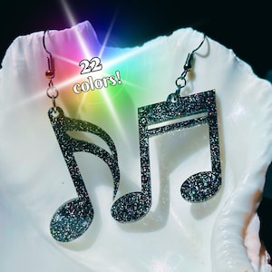 May include: A pair of silver glitter musical note earrings. The earrings are shaped like a treble clef and a quarter note. The text "22 colours!" is visible in the image.