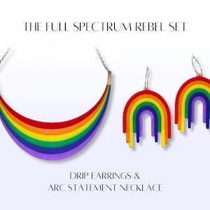 May include: A rainbow-colored arc statement necklace and matching drip earrings. The jewelry set features a vibrant spectrum of colors, including red, orange, yellow, green, blue, and purple. The text reads "THE FULL SPECTRUM REBEL SET" and "DRIP EARRINGS & ARC STATEMENT NECKLACE."