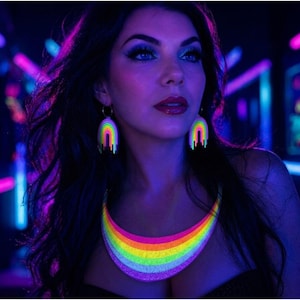May include: A woman wearing a rainbow-colored necklace and matching earrings. The jewelry glows brightly under blacklight, with a neon rainbow design. The background is dark with neon lights.