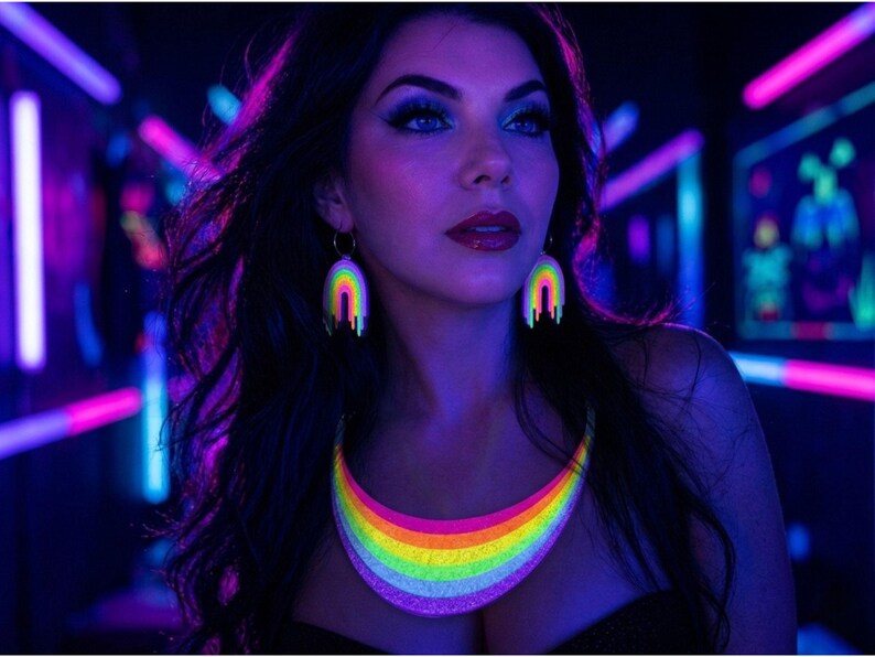 May include: A woman wearing a rainbow-colored necklace and matching earrings. The jewelry glows brightly under blacklight, with a neon rainbow design. The background is dark with neon lights.
