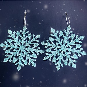 May include: A pair of snowflake-shaped earrings with a silver hoop and a light blue glitter finish.