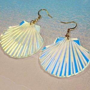 May include: A pair of iridescent white seashell earrings with gold hooks. The earrings are shaped like a scallop shell with a textured surface.