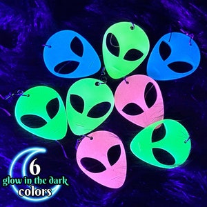 May include: Six pairs of glow-in-the-dark alien face earrings in pink, green, and blue.