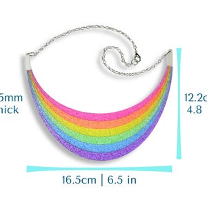 May include: A rainbow-colored glitter necklace with a silver chain. The necklace is 6.5 inches wide, 4.8 inches tall, and 4.5mm thick. The rainbow design features bands of pink, orange, yellow, green, blue, and purple.