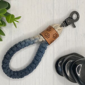May include: A blue and white rope dog leash with a brown leather paw print accent and a silver metal clip.