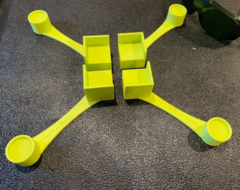 May include: A yellow plastic toy with four square compartments and four arms with round ends. The toy is on a black surface.