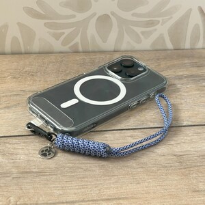 May include: A clear phone case with a white ring on the back. A blue and white braided phone strap with a paw print charm is attached to the case.