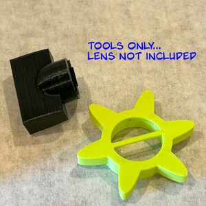 May include: A black plastic 3D printed tool and a bright green 3D printed star-shaped tool. The text "TOOLS ONLY... LENS NOT INCLUDED" is visible in the image.