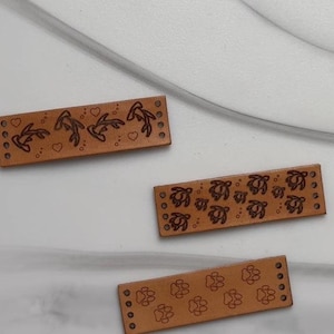 May include: Three leather straps with different designs. The first strap has a design of stylized fish and hearts. The second strap has a design of stylized sea turtles. The third strap has a design of paw prints.