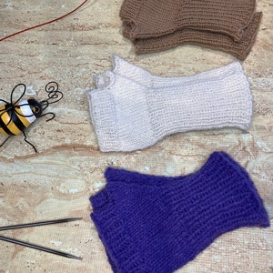 Puede incluir: Tres pares de guantes sin dedos de diferentes colores: marrón, blanco y morado. Los guantes están tejidos y tienen una textura acanalada.