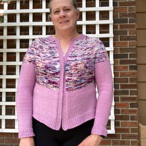 May include: A light purple cardigan with a V-neck and long sleeves. The upper chest area features a colorful, speckled pattern in shades of purple, pink, and blue. The sleeves and lower body are a solid light purple color.