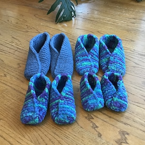 May include: Six pairs of crocheted slippers in two different colors. Two pairs are solid blue, two pairs are a blue and purple mix, and two pairs are a blue, green, and purple mix.