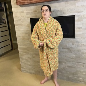 Może przedstawiać: Długa, żółta, pomarańczowa i zielona dzianinowa szlafrok z kapturem. Szlafrok jest związany w talii paskiem.