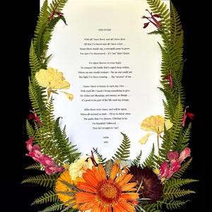 May include: A framed artwork featuring a poem titled "DISCOVERY" surrounded by a wreath of dried flowers and ferns. The arrangement includes vibrant orange, yellow, and pink blooms, set against a black background. The poem is written in black ink.